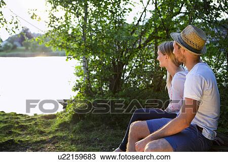 Mid adult couple sitting by lake watching sunset View Large Photo Image Stock Image - Mid adult couple sitting by lake watching sunset. Fotosearch