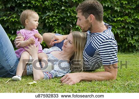 Mid adult couple with baby daughter reclining on lawn in garden View Large Photo Image Stock Image - Mid adult couple with baby daughter reclining on lawn in garden. Fotosearch