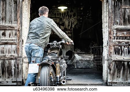Mid adult man pushing motorcycle into barn View Large Photo Image Stock Photo - Mid adult man pushing motorcycle into barn. Fotosearch