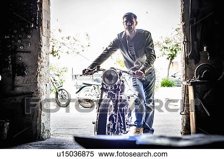 Mid adult man pushing motorcycle through barn doorway View Large Photo Image Stock Photography - Mid adult man pushing motorcycle through barn doorway. Fotosearch