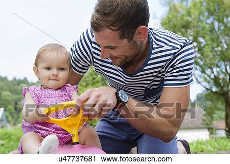 Mid adult man with baby daughter on toy car in garden View Large Photo Image Stock Image - Mid adult man with baby daughter on toy car in garden. Fotosearch