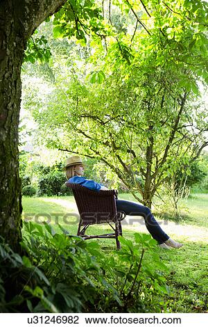 Stock Image - Mid adult woman asleep in garden chair. Fotosearch