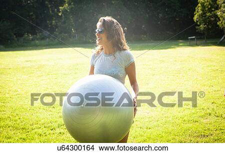 Picture - Mid adult woman holding up exercise ball in field. Fotosearch