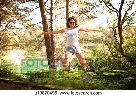 Stock Photograph - Mid adult woman jumping mid air, Blue Pool, Wareham, Dorset, UK. Fotosearch