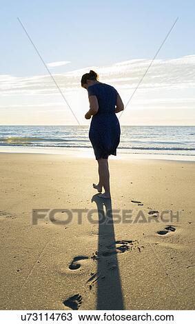 Stock Image - Mid adult woman making footprint in sand at coast, Westkapelle, Zeeland, Netherlands. Fotosearch