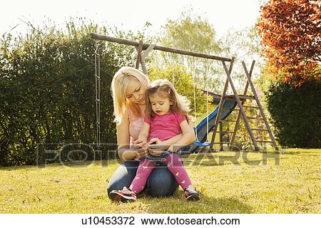 Stock Image - Mother and daughter in garden, swings in background. Fotosearch