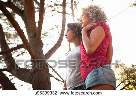 Stock Image - Mother and daughter looking into distance, tree in background. Fotosearch