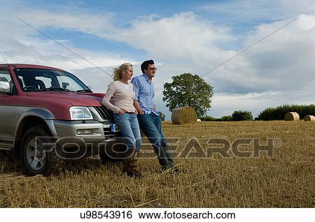 Stock Photograph - Mother and son leaning against four wheeled drive in harvested field. Fotosearch