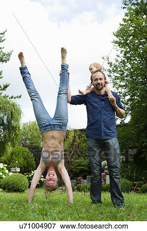 Mother doing handstand in garden next to family View Large Photo Image Stock Photo - Mother doing handstand in garden next to family. Fotosearch