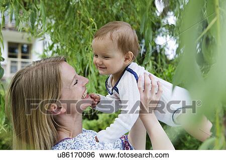 Mother holding up baby daughter face to face in garden View Large Photo Image Stock Photograph - Mother holding up baby daughter face to face in garden. Fotosearch