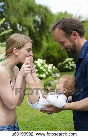 Stock Image - Mother kissing baby daughters feet in garden. Fotosearch