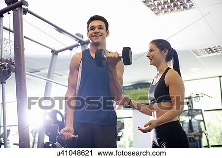 Stock Image - Personal trainer helping young man lift hand weights. Fotosearch