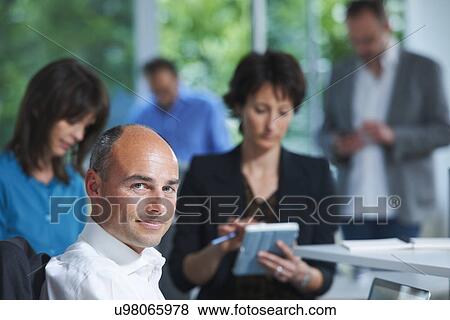 Portrait of businessman in front of colleagues in office View Large Photo Image Stock Photo - Portrait of businessman in front of colleagues in office. Fotosearch