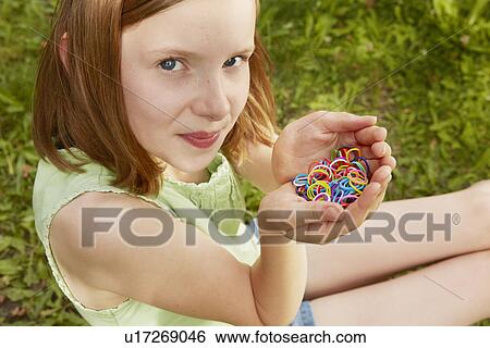 Stock Photograph - Portrait of girl in garden holding up rubber bands. Fotosearch