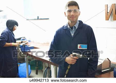 Stock Image - Portrait of male student with hand drill in college metalwork workshop. Fotosearch