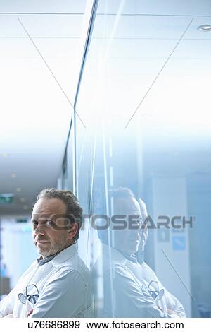 Stock Photo - Portrait of mature businessman leaning against glass wall in office. Fotosearch
