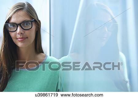Stock Photo - Portrait of mid adult businesswoman leaning against glass wall in office. Fotosearch