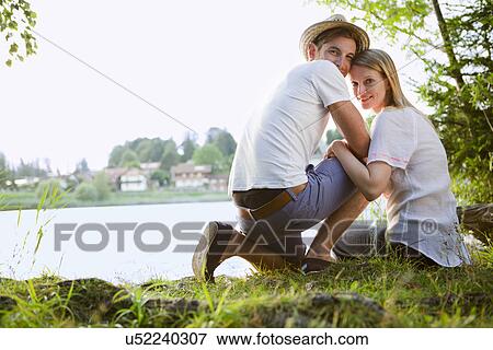 Portrait of mid adult couple sitting by lake looking back View Large Photo Image Stock Photo - Portrait of mid adult couple sitting by lake looking back. Fotosearch