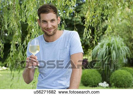 Stock Image - Portrait of mid adult man holding up a glass of white wine in garden. Fotosearch
