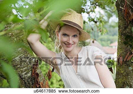 Stock Photography - Portrait of mid adult woman in straw hat next to garden tree. Fotosearch