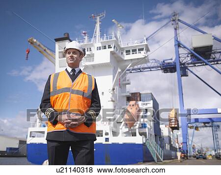 Stock Photo - Portrait of ship's captain standing in front of container ship. Fotosearch