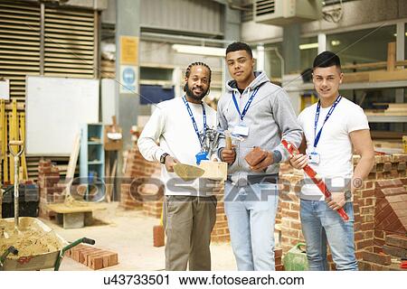 Stock Image - Portrait of three male college students in bricklaying workshop. Fotosearch