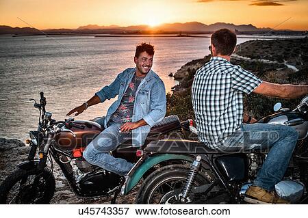 Portrait of two male motorcyclist friends on coast at sunset, Cagliari, Sardinia, Italy View Large Photo Image Stock Photo - Portrait of two male motorcyclist friends on coast at sunset, Cagliari, Sardinia, Italy. Fotosearch
