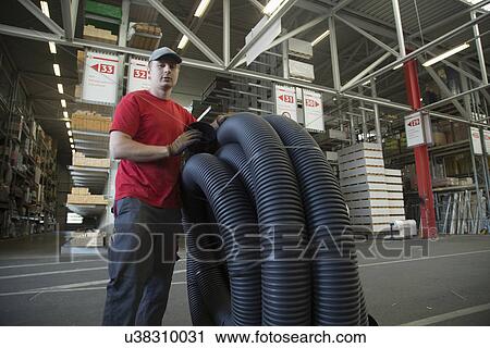 Stock Image - Portrait of worker with rolled up piping in hardware store warehouse. Fotosearch