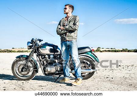Stock Image - Portrait of young male motorcyclist on arid plain, Cagliari, Sardinia, Italy. Fotosearch