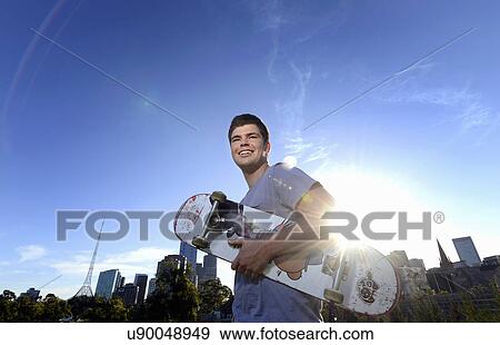 Stock Photo - Portrait of young man holding skateboard. Fotosearch