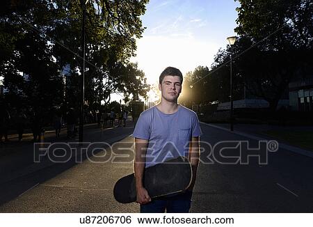 Stock Photograph - Portrait of young man holding skateboard. Fotosearch