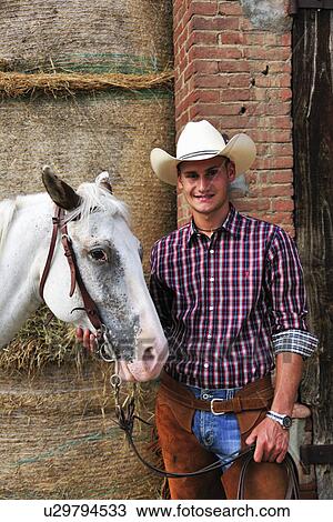 Portrait of young man in cowboy gear with horse outside stable View Large Photo Image Stock Image - Portrait of young man in cowboy gear with horse outside stable. Fotosearch