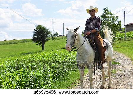 Stock Photograph - Portrait of young man in cowboy gear riding horse on rural road. Fotosearch