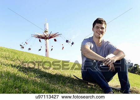 Portrait of young man sitting on skateboard View Large Photo Image Stock Photo - Portrait of young man sitting on skateboard. Fotosearch