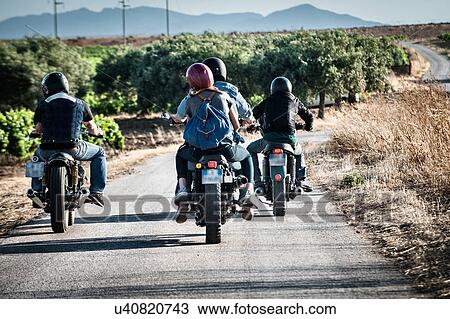 Stock Image - Rear view of four friends motorcycling on rural road, Cagliari, Sardinia, Italy. Fotosearch