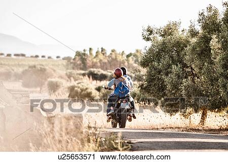 Rear view of mid adult couple riding motorcycle on dusty rural road, Cagliari, Sardinia, Italy View Large Photo Image Stock Image - Rear view of mid adult couple riding motorcycle on dusty rural road, Cagliari, Sardinia, Italy. Fotosearch