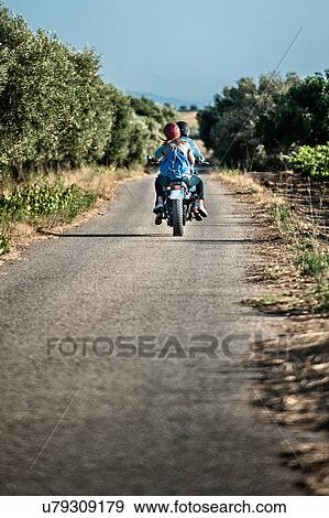 Rear view of mid adult couple riding motorcycle on rural road, Cagliari, Sardinia, Italy View Large Photo Image Stock Photo - Rear view of mid adult couple riding motorcycle on rural road, Cagliari, Sardinia, Italy. Fotosearch