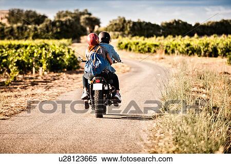 Rear view of mid adult couple riding motorcycle on winding rural road, Cagliari, Sardinia, Italy View Large Photo Image Stock Photography - Rear view of mid adult couple riding motorcycle on winding rural road, Cagliari, Sardinia, Italy. Fotosearch