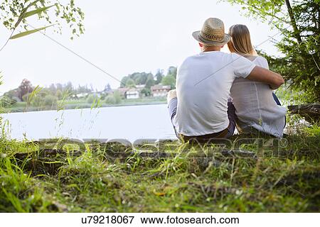 Rear view of mid adult couple sitting by lake View Large Photo Image Stock Photo - Rear view of mid adult couple sitting by lake. Fotosearch