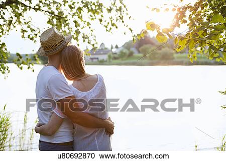 Rear view of mid adult couple watching sunset over lake View Large Photo Image Stock Image - Rear view of mid adult couple watching sunset over lake. Fotosearch