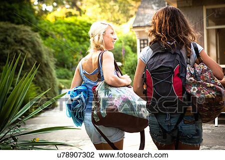 Stock Image - Rear view of two female friends out walking with backpack and bags. Fotosearch
