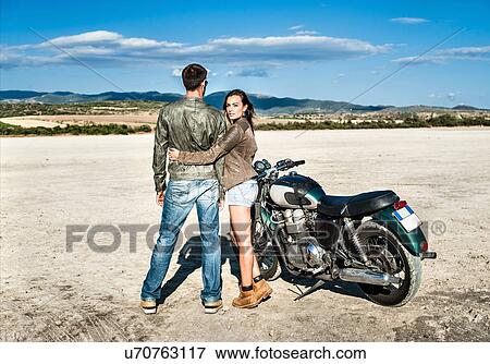 Stock Photo - Rear view of young couple and motorcycle on arid plain, Cagliari, Sardinia, Italy. Fotosearch
