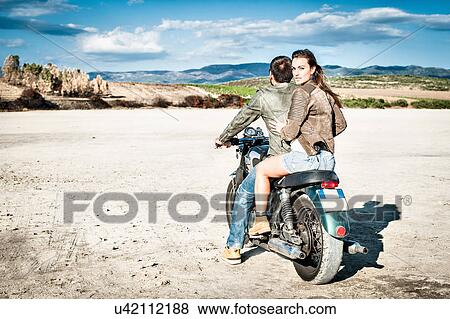 Rear view of young couple riding motorcycle on arid plain, Cagliari, Sardinia, Italy View Large Photo Image Stock Photo - Rear view of young couple riding motorcycle on arid plain, Cagliari, Sardinia, Italy. Fotosearch