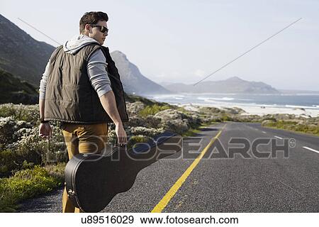 Rear view of young man walking on coastal road carrying guitar case, Cape Town, Western Cape, South Africa View Large Photo Image Stock Photo - Rear view of young man walking on coastal road carrying guitar case, Cape Town, Western Cape, South Africa. Fotosearch