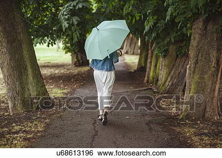 Rear view of young woman with umbrella strolling in park View Large Photo Image Stock Photograph - Rear view of young woman with umbrella strolling in park. Fotosearch