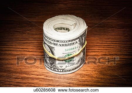 Stock Photo - Roll of american dollar notes wrapped in elastic band on office desk. Fotosearch