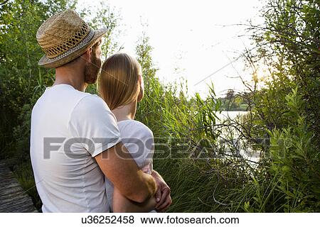 Romantic mid adult couple watching lakeside sunset View Large Photo Image Stock Photo - Romantic mid adult couple watching lakeside sunset. Fotosearch
