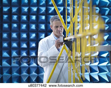 Stock Image - Scientist in lab coat preparing to measure electromagnetic waves in anechoic chamber. Fotosearch