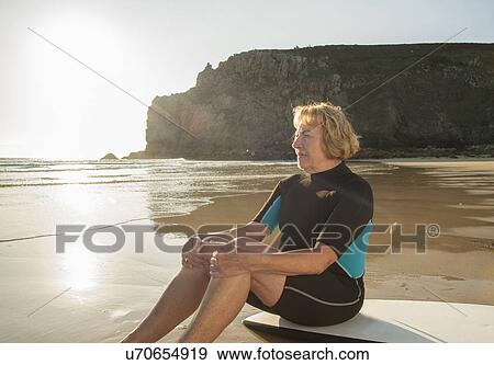 Stock Photo - Senior woman surfer sitting on surfboard, Camaret-sur-mer, Brittany, France. Fotosearch