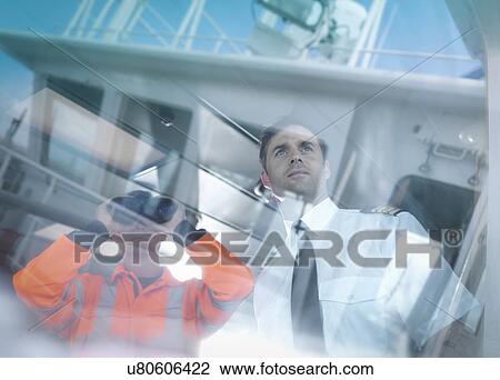 Stock Image - Ship's captain and worker seen through reflections on container ship. Fotosearch